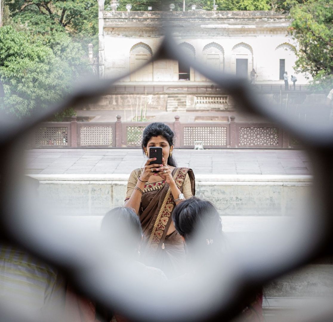 Frau fotografiert durch ein ornamentales Gitter vor historischer Architektur