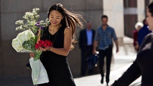 Frau mit Blumenstrauß in einer belebten Straße, im Vorübergehen fotografiert