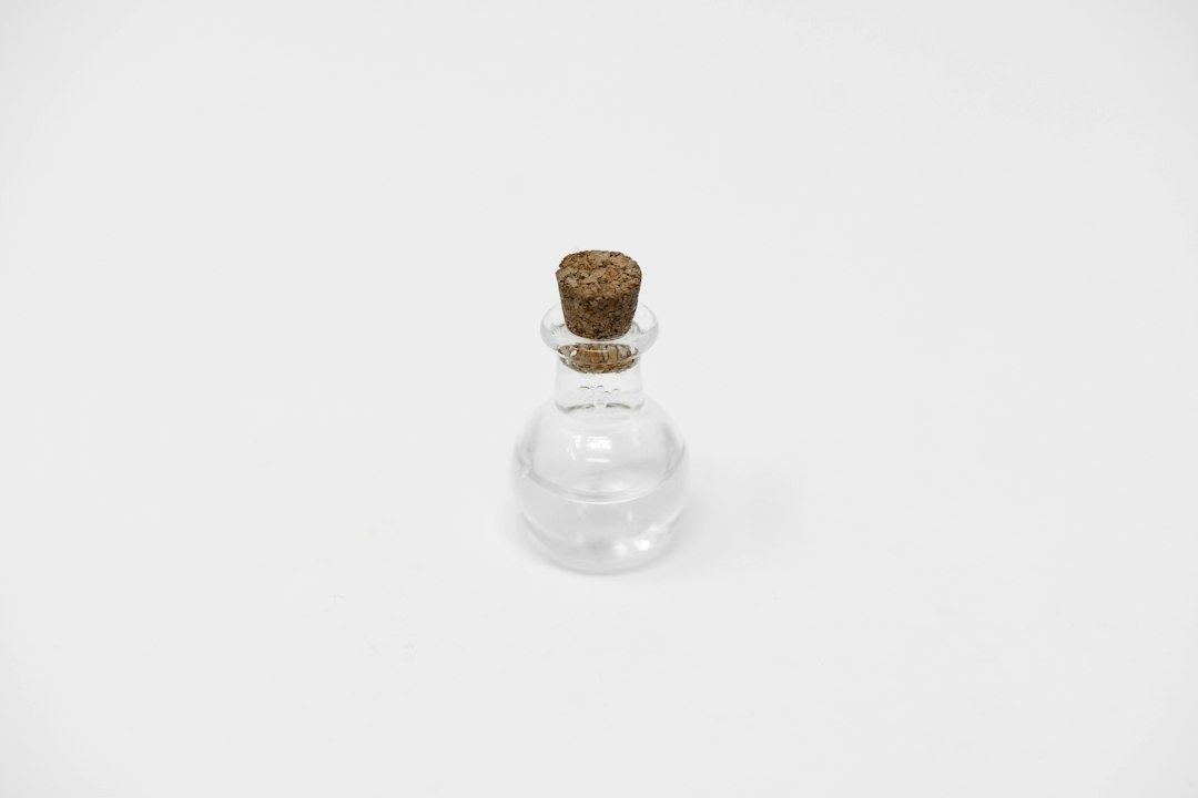 Kleine Glasflasche mit Korken vor weitgehend leerem weißem Hintergrund